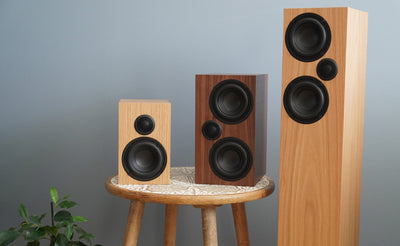 The Ophidian M-Series bookshelf and tower speakers  with a wooden finish on a blue background.